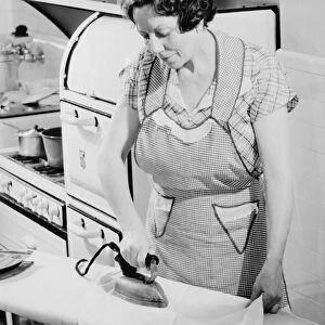 Woman ironing in kitchen, (B&W)