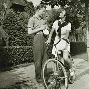 Young couple talking on street, woman on bicycle, (B&W)