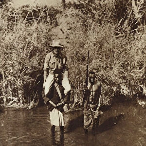 African porter carrying an explorer across the shallow River Nicadgi in Mozambique (b / w photo)