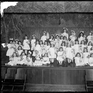 Group of little girls posed on a small stage holding dolls