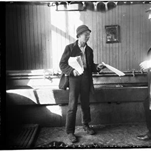 Portrait of a newsboy handing a paper to a man in what apperas to be a restroom at