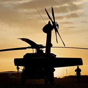 A UH-60L Black Hawk helicopter silhouetted by the setting sun