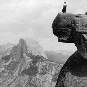 Historic image in black and white of a woman standing on a high cliff at Yosemite National Park; California, United States of America