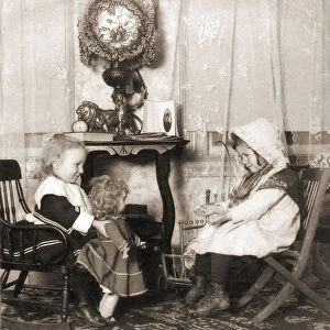 Two young girls playing dress-up with a doll, Victorian era circa 1903