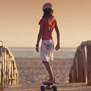 A Young Person Skateboarding With Bare Feet Over A Wooden Boardwalk Towards The Beach; Tarifa, Cadiz, Andalusia, Spain