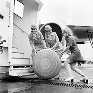 3 air hostesses rolling along a wheel of some sort A 2 Local Caption