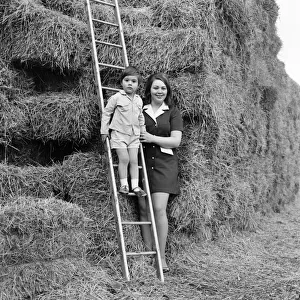 A woman outside with her son standing by a large haystack
