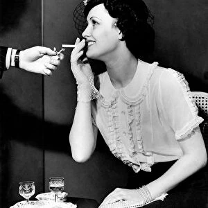 A woman about to smoke a cigarette, receives a light from a man