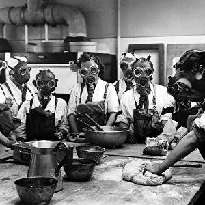 Women wearing gas masks while watching a cookery. June 1941