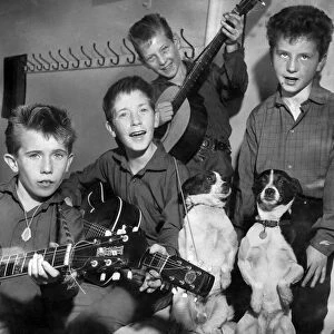 Young group of boys holding their guitars as they practice watched by their pet dogs
