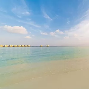 Amazing Maldives scenery, water villas and beach umbrella with palm trees. Tranquil sunset landscape in tropical beach. Luxury vacation destination