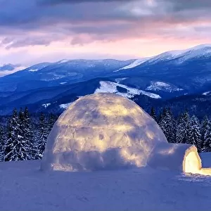 Real snow igloo house in the winter mountains. Snow-covered firs and mountain peaks on the background. Foggy forest with snowy spruce