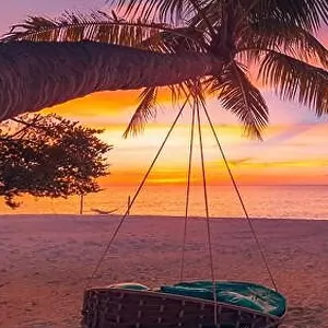 Tropical sunset beach background as summer coast landscape panorama with leisure beach swing on palm, white sand and calm sea beach horizon