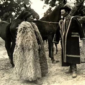 Two men, in traditional Hungarian dresses, are talking with each other; behind, a third man keeps some horses in the snare
