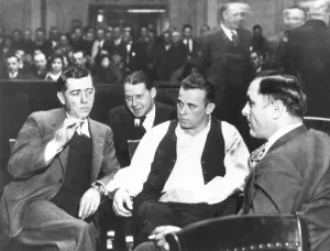 JOHN DILLINGER (1903-1934). American bank robber. Dillinger (wearing open vest) surrounded by guards at his arraignment in court in Crown Point, Indiana, on 9 February, 1934, on the charge of killing a policeman in East Chicago, Indiana JOHN DILLINGER (1903-1934). American bank robber. Dillinger (wearing open vest) surrounded by guards at his arraignment in court in Crown Point, Indiana, on 9 February, 1934, on the charge of killing a policeman in East Chicago, Indiana